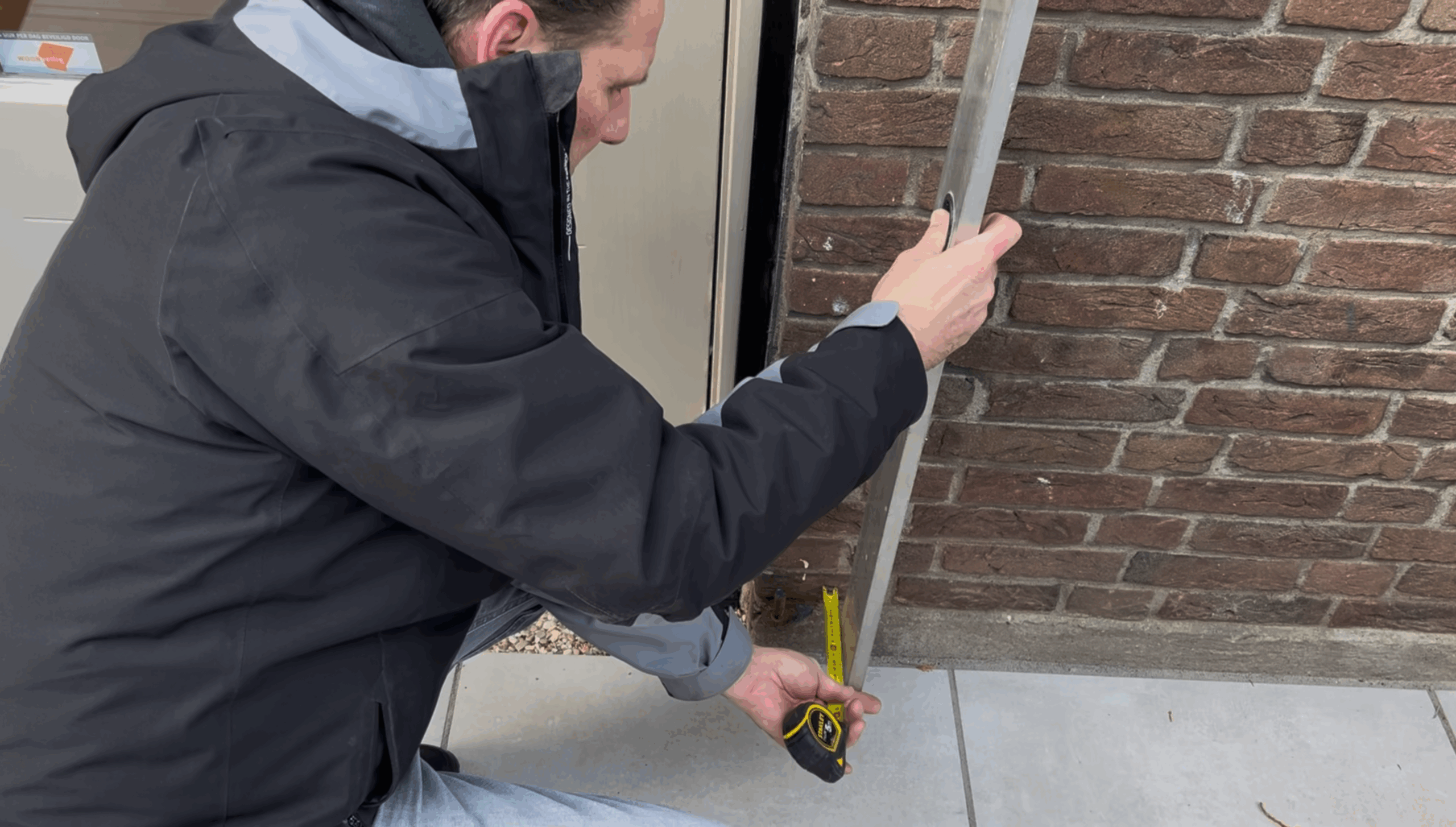 Loodmeting waarbij een adviseur met een waterpas de scheefstand van een gevel verticaal controleert