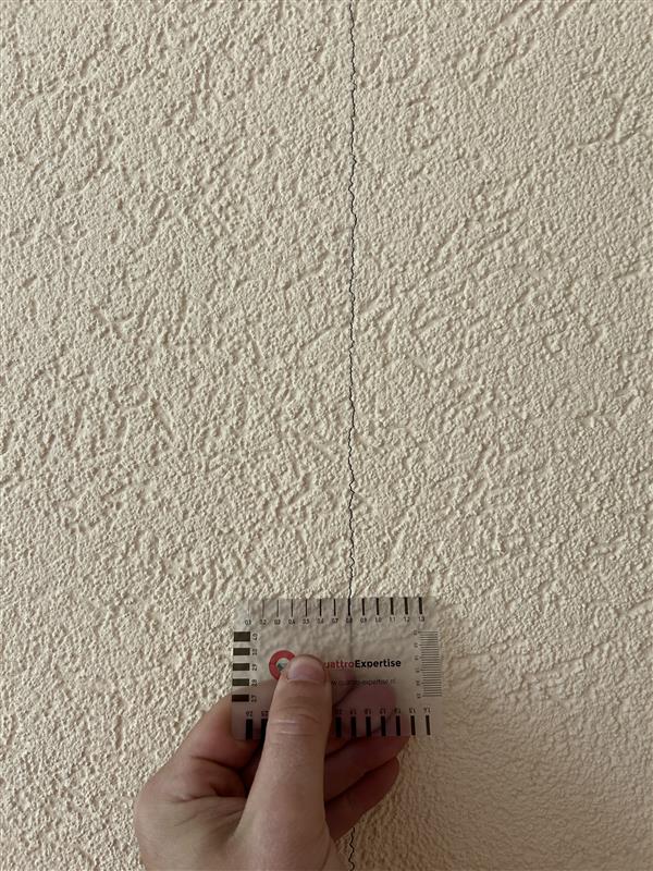 Een scheur in een gestucte muur wordt met een scheurwijdtemeter vastgelegd