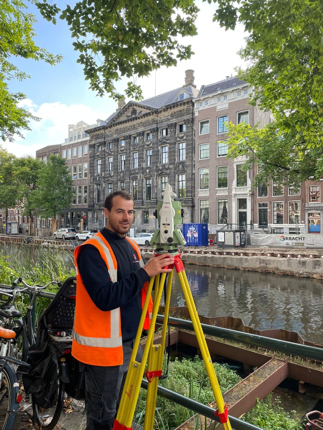 Landmeter met meetinstrument op statief langs een gracht